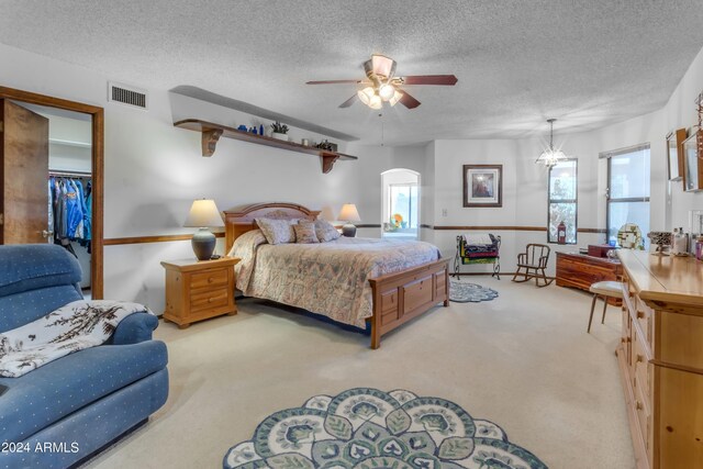 carpeted bedroom featuring ceiling fan with notable chandelier and a textured ceiling