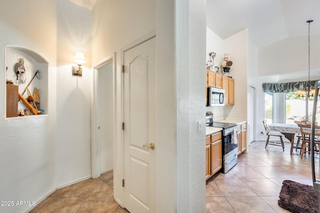 kitchen featuring decorative light fixtures, high vaulted ceiling, light brown cabinets, light tile patterned floors, and stainless steel appliances