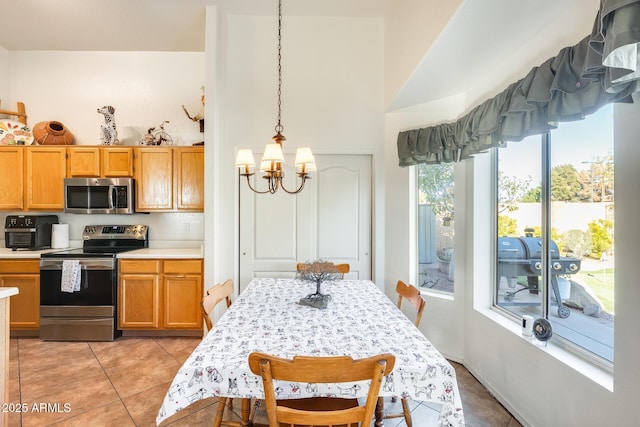 kitchen with an inviting chandelier, hanging light fixtures, light tile patterned floors, appliances with stainless steel finishes, and a high ceiling