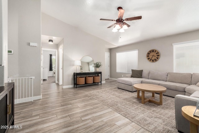 living area featuring vaulted ceiling, ceiling fan, light wood finished floors, and baseboards