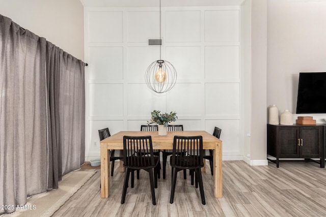 dining room featuring visible vents, a decorative wall, and light wood-style flooring