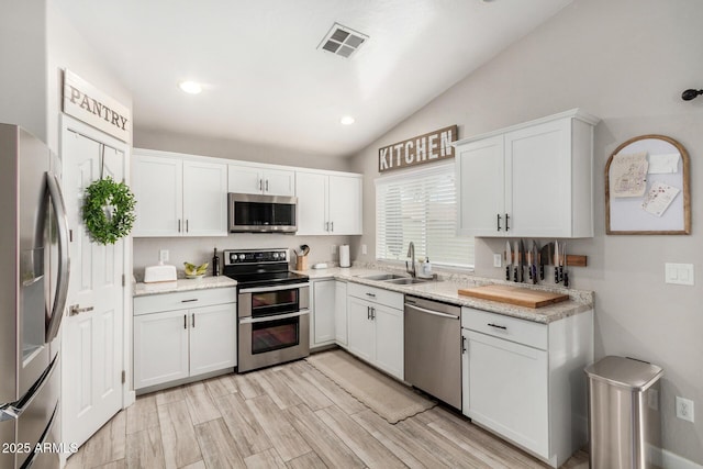 kitchen featuring visible vents, appliances with stainless steel finishes, white cabinets, vaulted ceiling, and a sink