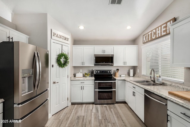 kitchen featuring visible vents, white cabinets, lofted ceiling, stainless steel appliances, and a sink