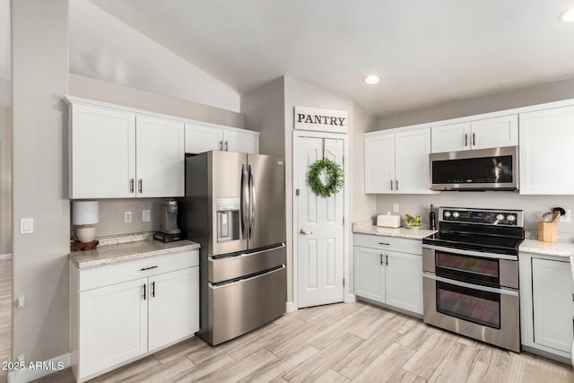 kitchen featuring stainless steel appliances, lofted ceiling, recessed lighting, light wood-style floors, and white cabinets