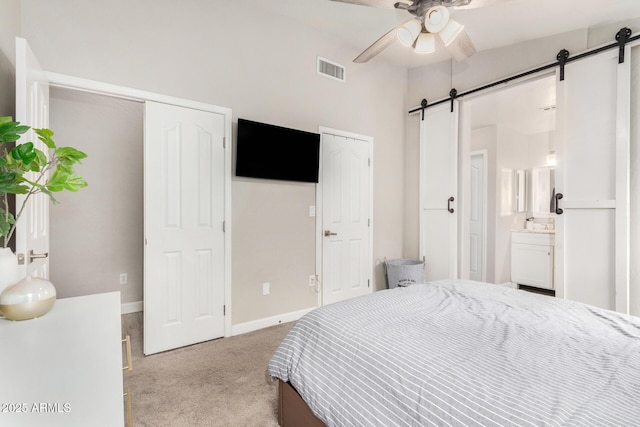 bedroom featuring visible vents, a barn door, carpet flooring, ensuite bath, and baseboards