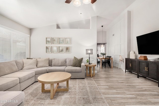 living room with ceiling fan, high vaulted ceiling, and light wood-style floors