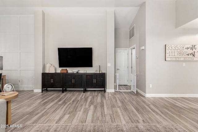 living room featuring baseboards, a high ceiling, visible vents, and light wood-style floors