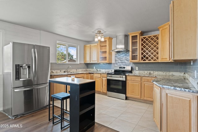 5802 N 61st Dr, Glendale, AZ 85301 - kitchen featuring appliances with stainless steel finishes, wall chimney range hood, light brown cabinetry, tasteful backsplash, and glass insert cabinets
