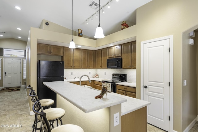 kitchen featuring visible vents, vaulted ceiling, black appliances, tasteful backsplash, and an island with sink