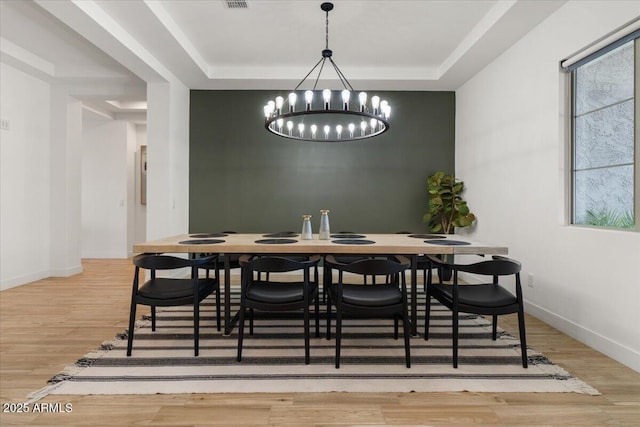 dining room featuring an inviting chandelier, baseboards, a tray ceiling, and wood finished floors