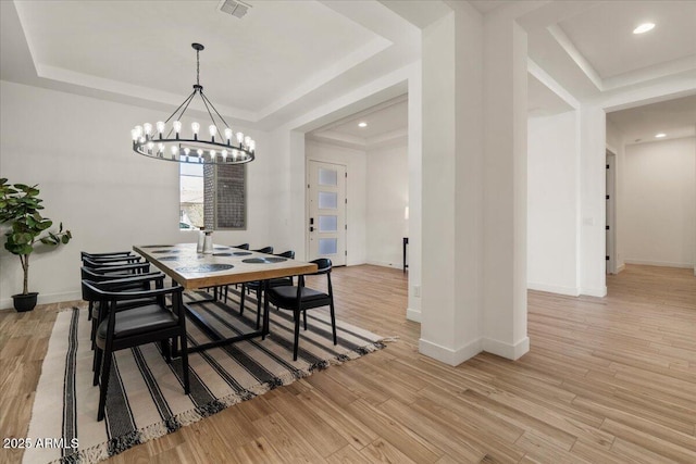 dining area featuring a tray ceiling, a notable chandelier, and light wood-style flooring