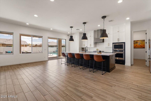 kitchen featuring a kitchen breakfast bar, wall chimney range hood, light countertops, tasteful backsplash, and stainless steel appliances