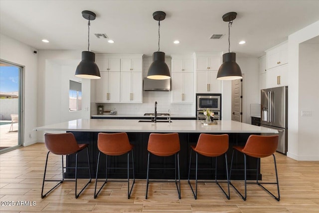 kitchen with wall chimney exhaust hood, stainless steel appliances, white cabinetry, decorative backsplash, and visible vents