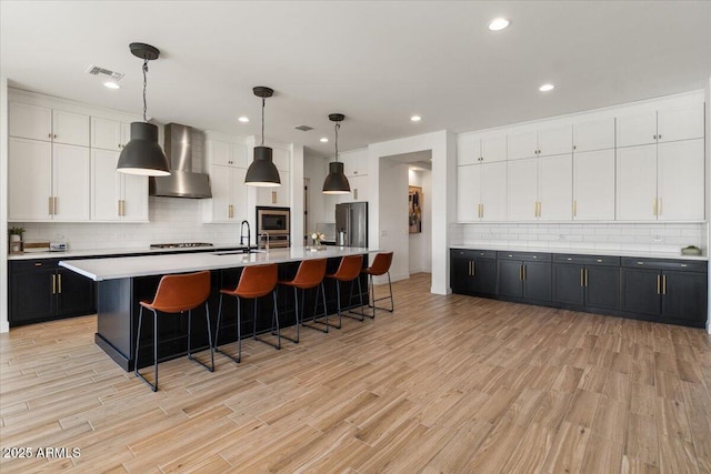 kitchen featuring stainless steel appliances, visible vents, white cabinetry, and wall chimney exhaust hood