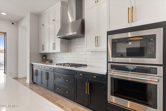 kitchen with light countertops, wall chimney exhaust hood, white cabinetry, light wood finished floors, and stainless steel appliances
