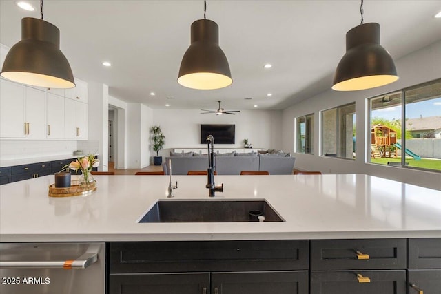 kitchen with hanging light fixtures, dishwasher, a sink, light countertops, and open floor plan