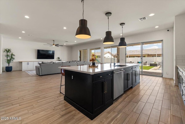 kitchen with a sink, light countertops, dark cabinets, light wood-type flooring, and visible vents