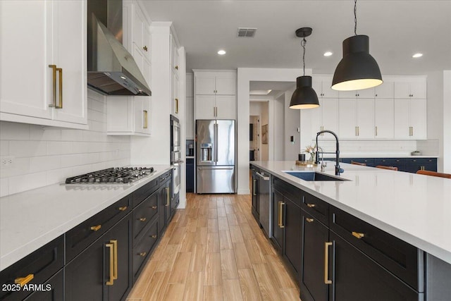 kitchen featuring wall chimney range hood, appliances with stainless steel finishes, light countertops, a sink, and white cabinetry