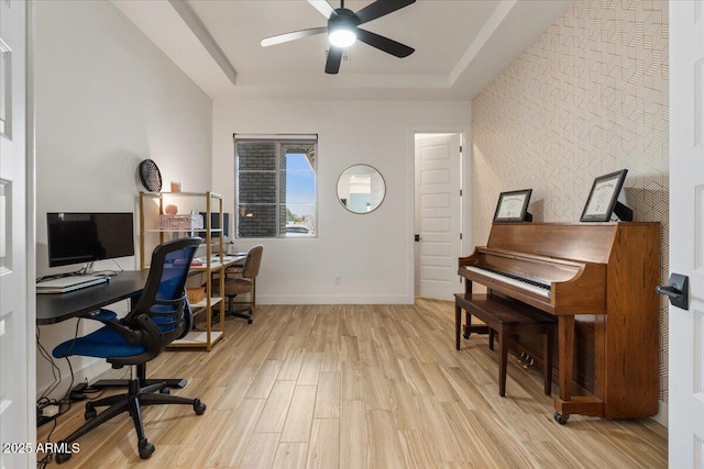 office space with baseboards, a tray ceiling, ceiling fan, and light wood-style floors