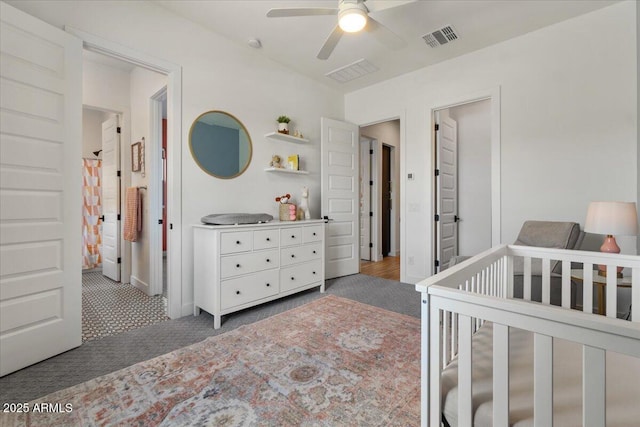 carpeted bedroom with a crib, ceiling fan, and visible vents