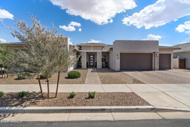 pueblo-style house featuring an attached garage, stucco siding, and decorative driveway