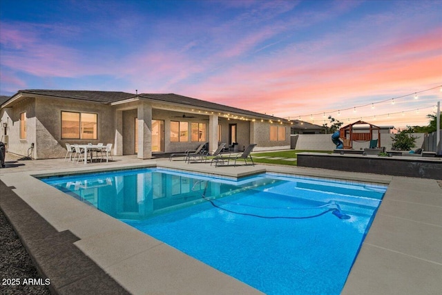 pool at dusk featuring a fenced in pool, fence, a patio, and a playground