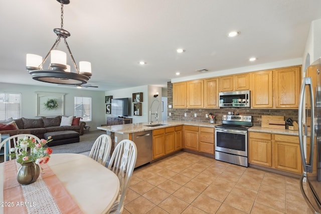 kitchen with a peninsula, a sink, stainless steel appliances, open floor plan, and tasteful backsplash