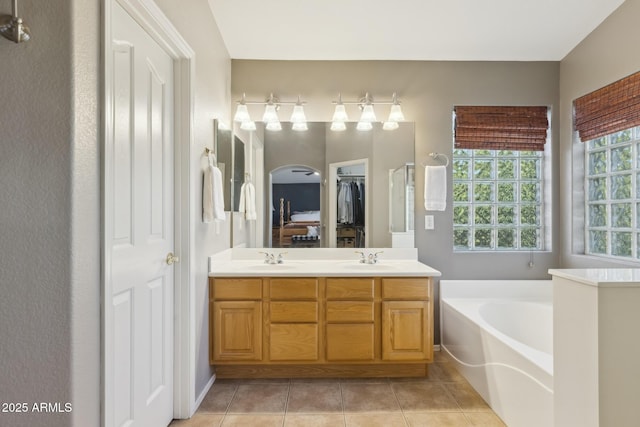 bathroom with tile patterned floors, a bath, double vanity, and a sink