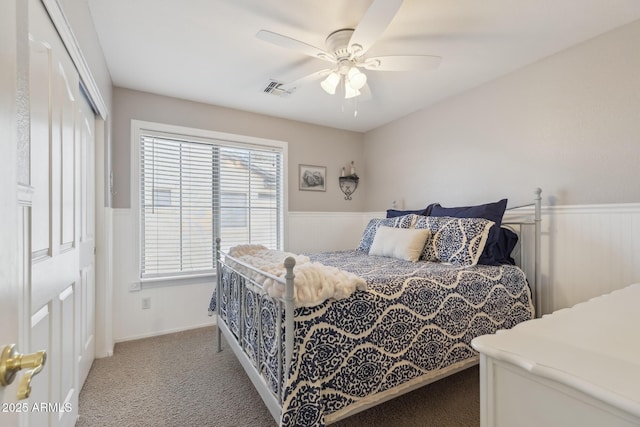 bedroom with visible vents, ceiling fan, carpet flooring, wainscoting, and a closet