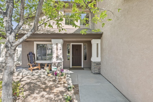 view of exterior entry with stucco siding, stone siding, roof with shingles, and a porch