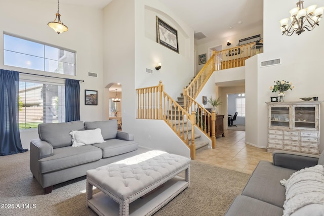 tiled living room with stairway, arched walkways, an inviting chandelier, and visible vents