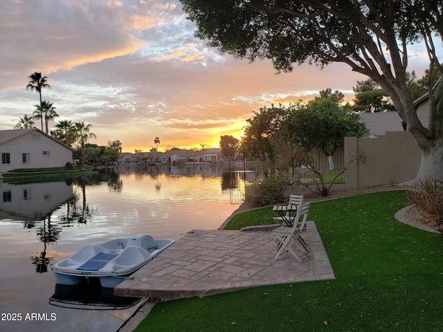 view of dock with a patio, a lawn, a water view, and fence