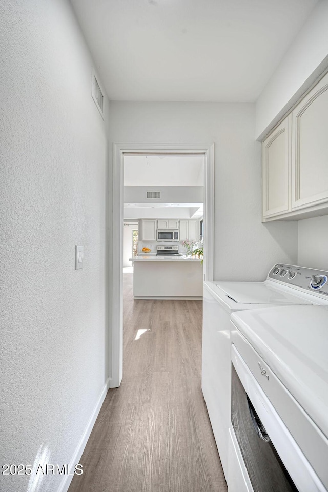 laundry area with cabinets, washing machine and clothes dryer, and light hardwood / wood-style flooring