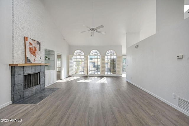 unfurnished living room featuring a tile fireplace, dark hardwood / wood-style floors, ceiling fan, and high vaulted ceiling