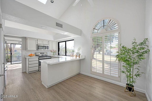 kitchen with sink, white cabinets, light hardwood / wood-style floors, kitchen peninsula, and stainless steel appliances