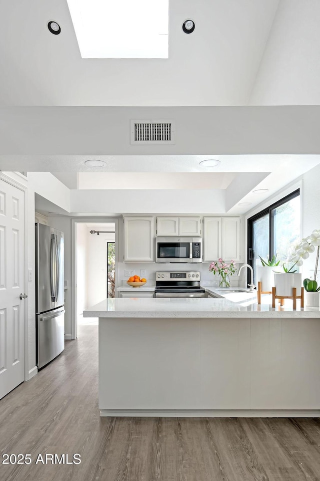 kitchen with a healthy amount of sunlight, a skylight, white cabinets, and appliances with stainless steel finishes