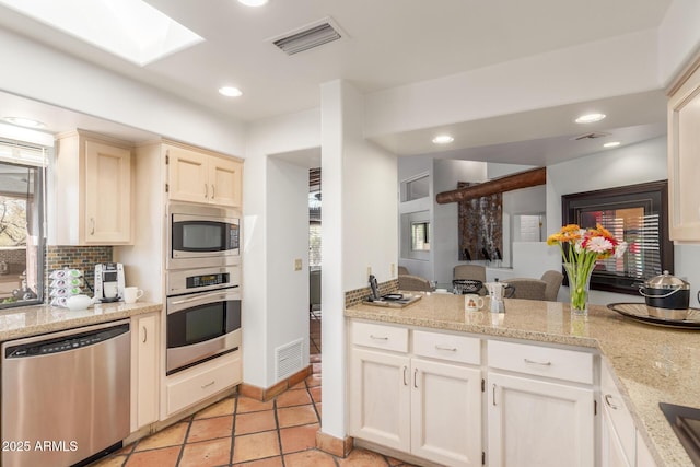 kitchen featuring light tile patterned floors, appliances with stainless steel finishes, a skylight, light stone countertops, and decorative backsplash