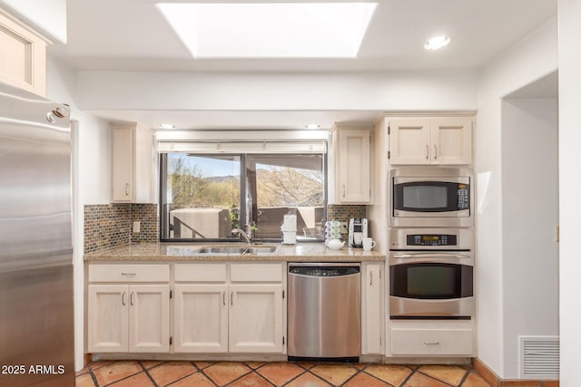 kitchen with light stone counters, sink, decorative backsplash, and stainless steel appliances