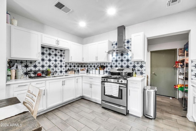 kitchen with stainless steel gas stove, sink, white cabinetry, and wall chimney exhaust hood