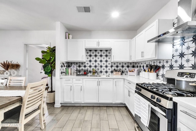 kitchen with wall chimney exhaust hood, sink, gas stove, white cabinetry, and decorative backsplash