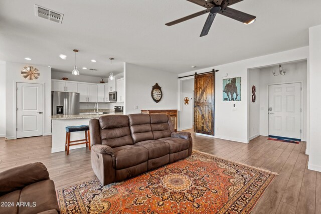 living room with ceiling fan, sink, light hardwood / wood-style floors, and a barn door