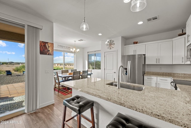 kitchen with white cabinets, sink, decorative light fixtures, stainless steel appliances, and light wood-type flooring