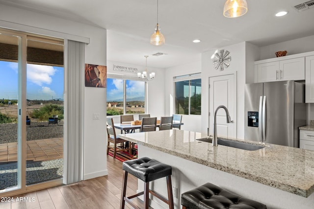 kitchen with light hardwood / wood-style floors, sink, white cabinets, hanging light fixtures, and stainless steel fridge