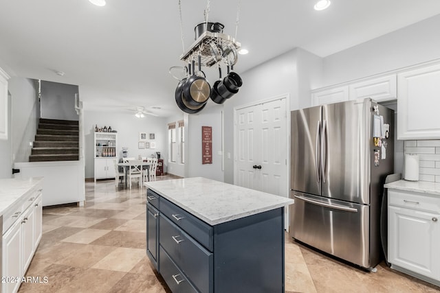 kitchen featuring light stone counters, backsplash, white cabinetry, stainless steel refrigerator, and a center island