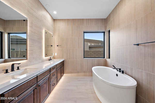 full bathroom featuring double vanity, a freestanding bath, tile walls, and a sink