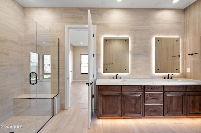 full bathroom with double vanity, a shower stall, a sink, and wood finished floors