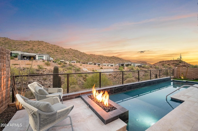 pool at dusk featuring a mountain view, a fire pit, fence, a fenced in pool, and a patio area