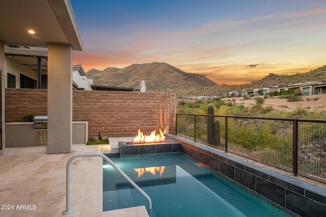 view of swimming pool with a fire pit, a grill, fence, exterior kitchen, and a mountain view