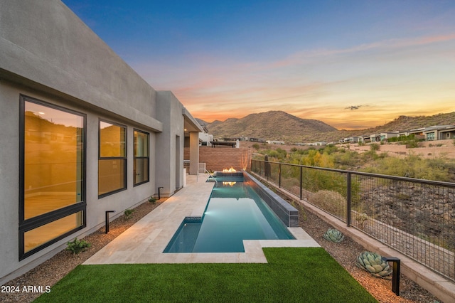 pool at dusk with a patio, a fenced backyard, a mountain view, a lawn, and a fenced in pool