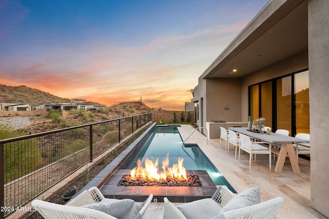 pool at dusk featuring outdoor dining area, a fenced backyard, a fenced in pool, a patio area, and an outdoor living space with a fire pit